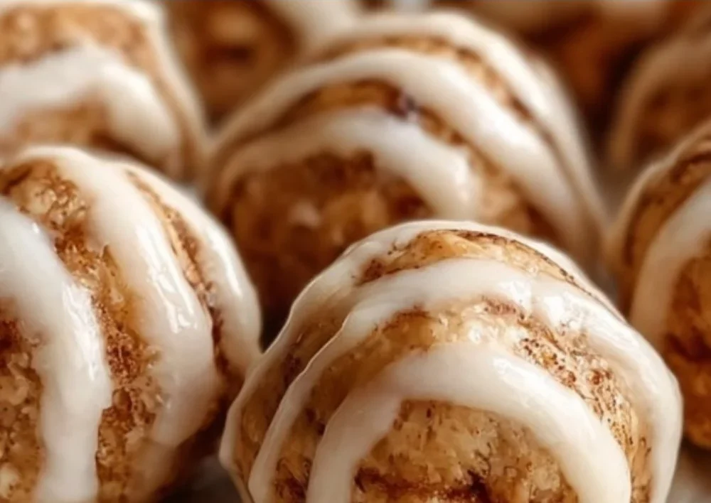 Cinnamon roll protein bites displayed on a wooden table with a sprinkle of cinnamon.
